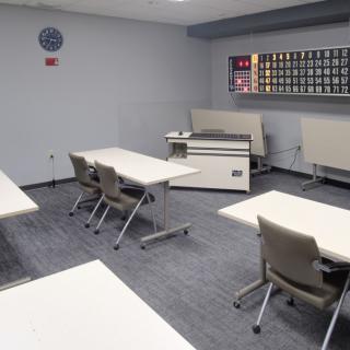 An empty classroom with desks and chairs arranged neatly, featuring a projector at the front.