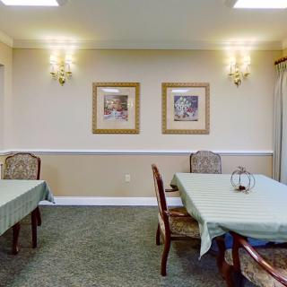 A cozy dining room with neatly arranged tables and chairs, adorned with framed artwork and elegant lighting.