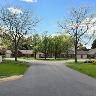 A serene residential neighborhood with houses lining a quiet street, surrounded by lush green trees.
