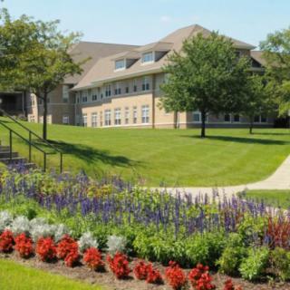 A scenic view of a building surrounded by a lush garden with colorful flowers and trees.