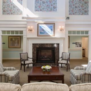 A cozy living room with a fireplace, surrounded by chairs and adorned with artwork and decor.