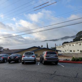 A serene morning view of a parking lot with cars parked and clouds hovering over the mountains in the background.