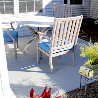 A cozy outdoor patio setup with a table and chairs, featuring blue cushions.