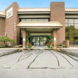 The entrance of a modern commercial building with a spacious parking area.