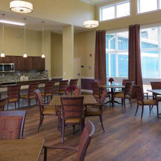 A modern dining area with wooden tables and chairs, featuring a kitchen in the background.