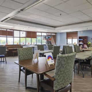 A spacious and inviting community dining area with tables and chairs arranged for social gatherings, illuminated by natural light from large windows.