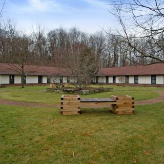 Circular courtyard with buildings and wooden benches surrounded by trees.