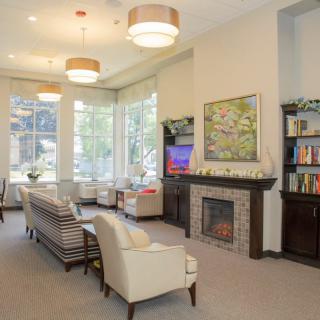 A bright and inviting living room with comfortable seating, a fireplace, bookshelves, and large windows.