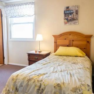 A cozy bedroom featuring a single bed with floral bedspread, a wooden headboard, and a nightstand with a lamp beside a window.