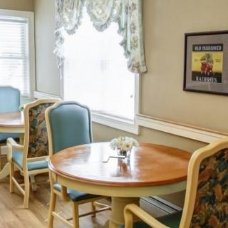 A cozy dining area with round tables and upholstered chairs near a window with elegant curtains.