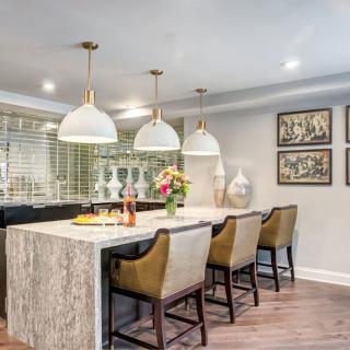A modern kitchen with a marble countertop, barstools, and pendant lighting, featuring decorative artwork and a vase of flowers.
