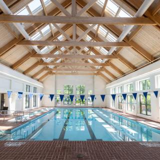 A well-lit indoor swimming pool with wooden beams and skylights.