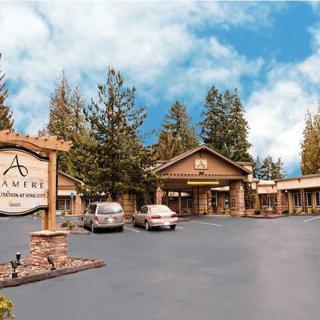 A view of a hotel exterior with a parking lot and cars, surrounded by trees under a blue sky.
