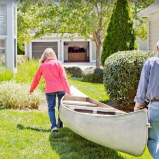 Two people carrying a canoe across a grassy backyard.