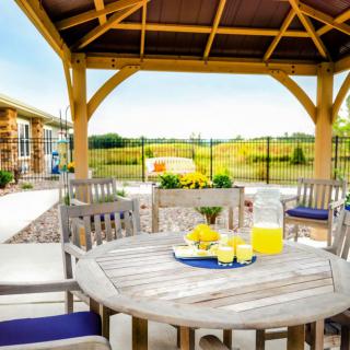 An inviting outdoor patio with a wooden seating area under a gazebo, featuring a table set with lemonade and surrounded by scenic landscape views.
