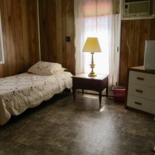 A cozy bedroom with a single bed, lamp, and dresser beside a curtained window.