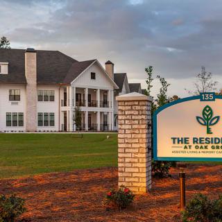 A large residential building with a sign in front, surrounded by a landscaped lawn and trees.