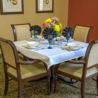 A neatly set dining table with a white tablecloth, surrounded by chairs and adorned with colorful flowers.