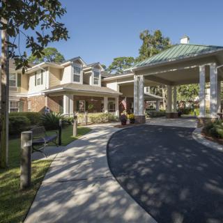A residential building with a covered porch and a curved driveway surrounded by trees.