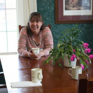 A woman sitting at a dining table with a plant and mugs.