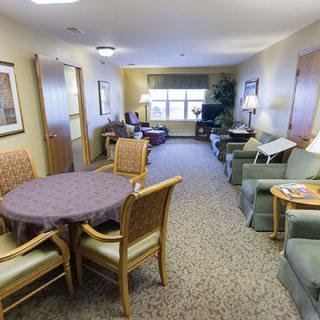 A cozy living room with seating area and a table, featuring sofas, chairs, and a window allowing natural light.