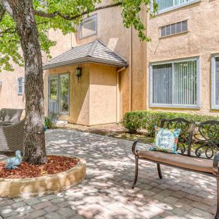 A peaceful courtyard with a bench under a tree, surrounded by a building and paved walkway.