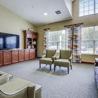 A spacious living room with a television, chairs, and large windows.