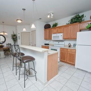 A modern kitchen with wooden cabinets, white appliances, and a dining area featuring bar stools at the counter.
