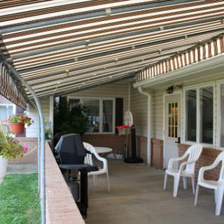A serene outdoor patio featuring a covered area with chairs and a grill, perfect for relaxation.