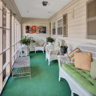 A cozy enclosed porch with wicker furniture and green carpeting, adorned with plants and decorative artwork.