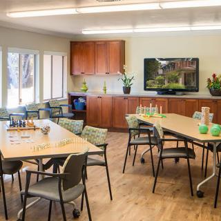A well-lit classroom with tables, chairs, and a television for learning activities.