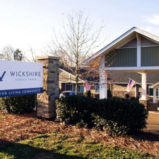 Entrance of the Wickshire senior living community with a sign and flags.