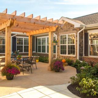 A cozy patio with a wooden pergola, outdoor seating, and vibrant flowers surrounded by a brick house.
