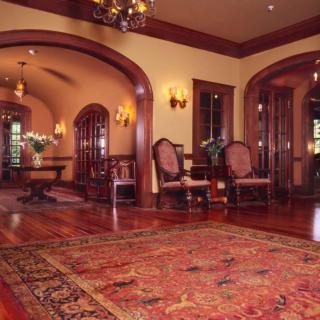 A grand lounge featuring traditional decor with wooden flooring, elegant arched doorways, and a large area rug.