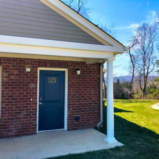 A small brick house with a blue door and white column under a clear, sunny sky.