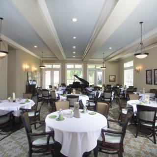 Elegant dining room with round tables, chairs, and a grand piano.