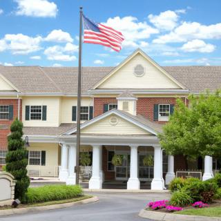 A stately building with an American flag at the entrance, surrounded by well-maintained landscaping under a partly cloudy sky.