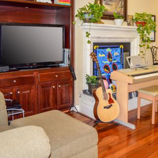 A cozy living room with a guitar, piano, and TV, complemented by plants and a fireplace.