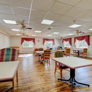 A spacious and well-lit dining area featuring wooden floors, tables, and chairs with ceiling fans.