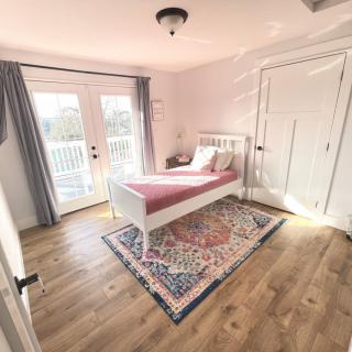 A bright, minimalist bedroom with a single bed and a colorful rug on a wooden floor.
