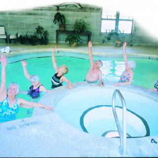 A group of elderly women participating in a water aerobics class in an indoor swimming pool.