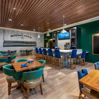 A modern restaurant interior with a bar and seating area, featuring wooden ceiling and green accents.