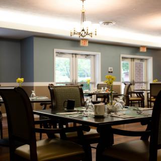 A cozy dining room with neatly arranged tables and chairs, illuminated by warm lighting.