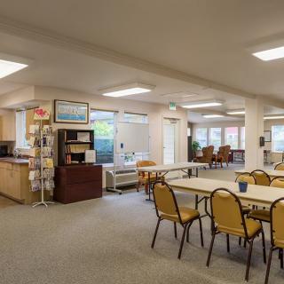 A spacious and bright common room with multiple tables and chairs arranged for social gatherings.