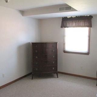 An empty room with a single dresser and a window with a curtain.