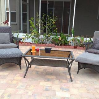 A cozy patio setup with two cushioned chairs and a glass-top table surrounded by greenery.