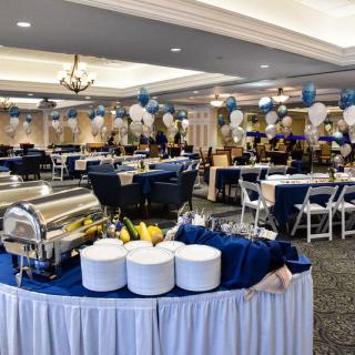 A beautifully decorated banquet hall ready for an event, featuring a buffet table and blue and white balloon decorations.