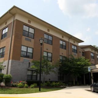 A multi-story residential building with a landscaped entrance and trees on a cloudy day.