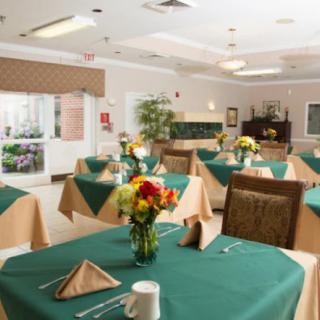 A cozy dining room with neatly arranged tables featuring green tablecloths and floral centerpieces.