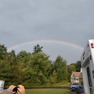 A beautiful rainbow arches over a lush green landscape, contrasting with the gray clouds above.
